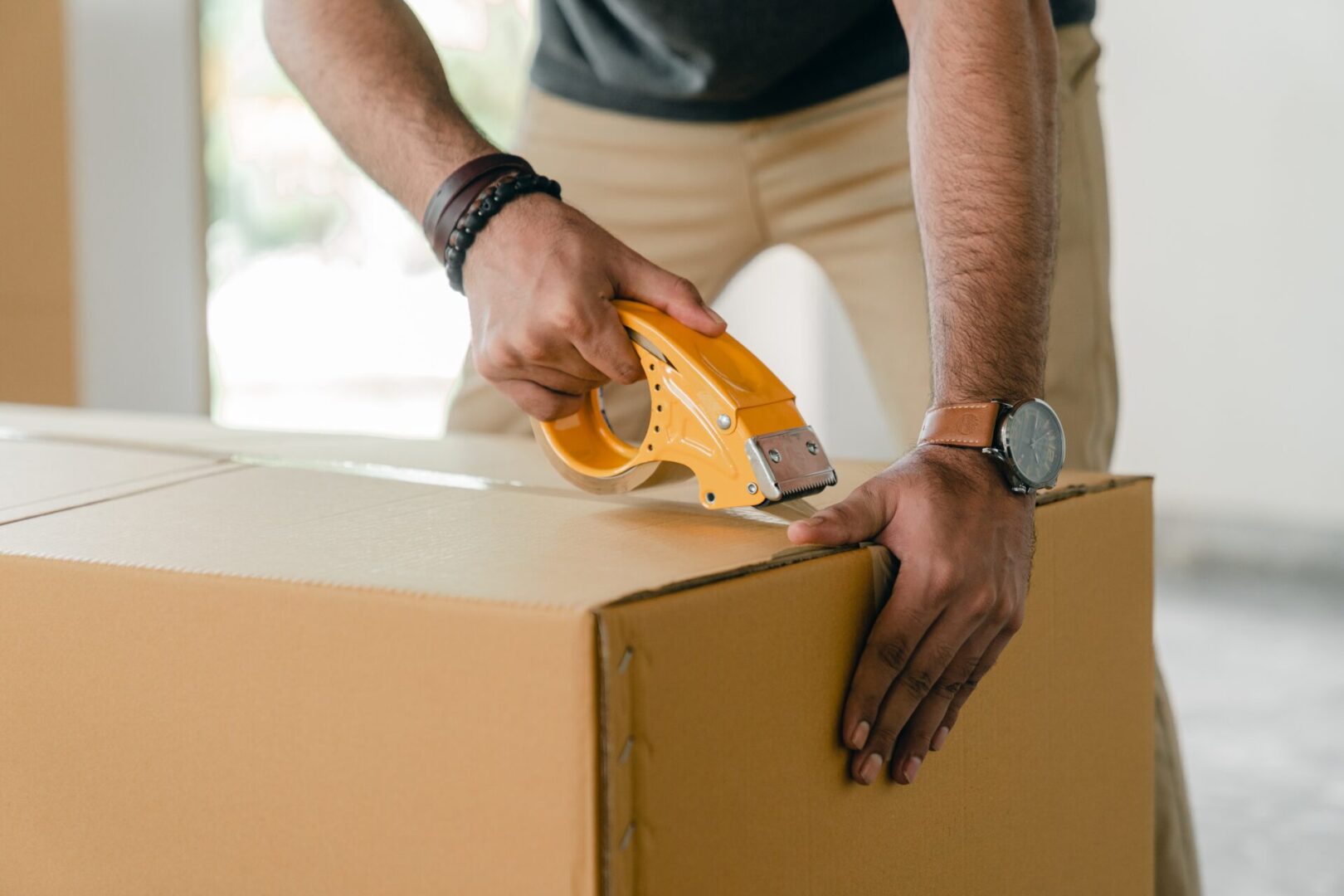 A person is cutting cardboard with an orange tape dispenser.